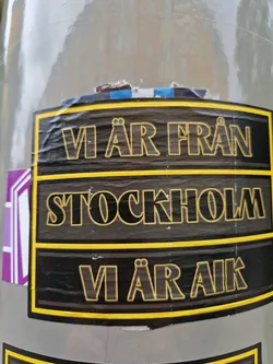 A black and yellow sticker with the text "Vi är från Stockholm. Vi är AIK."  The text is in Swedish and translates to "We are from Stockholm. We are AIK." AIK is likely a reference to AIK Fotboll, a Swedish football club.