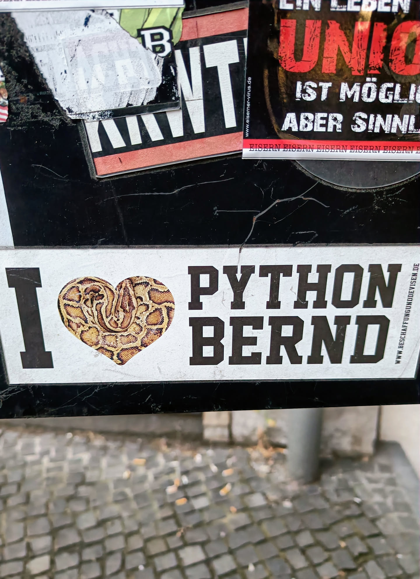 A sticker with a snake in the shape of a heart and the text 'I love Python Bernd'. The sticker has a website address at the bottom right corner.