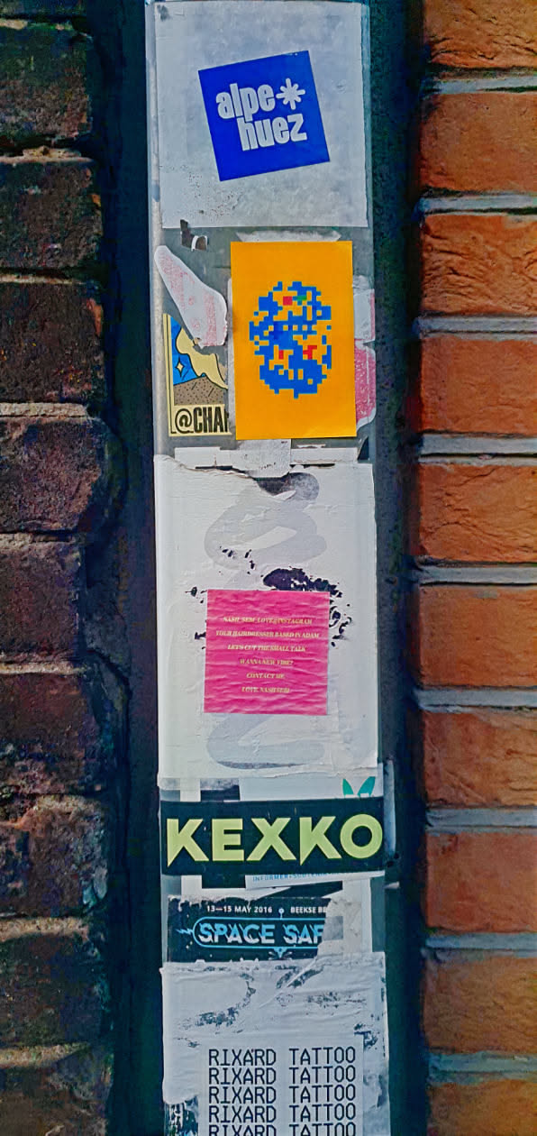 This image showcases a variety of stickers plastered on a wall. The collection includes a blue sticker with 'alpe*huez' text, a vibrant orange sticker displaying pixel art, and ads for 'RIXARD TATTOO'. There's also a 'KEXKO' sticker and a faded event poster. The composition captures the layered and accumulated effect of urban sticker art.