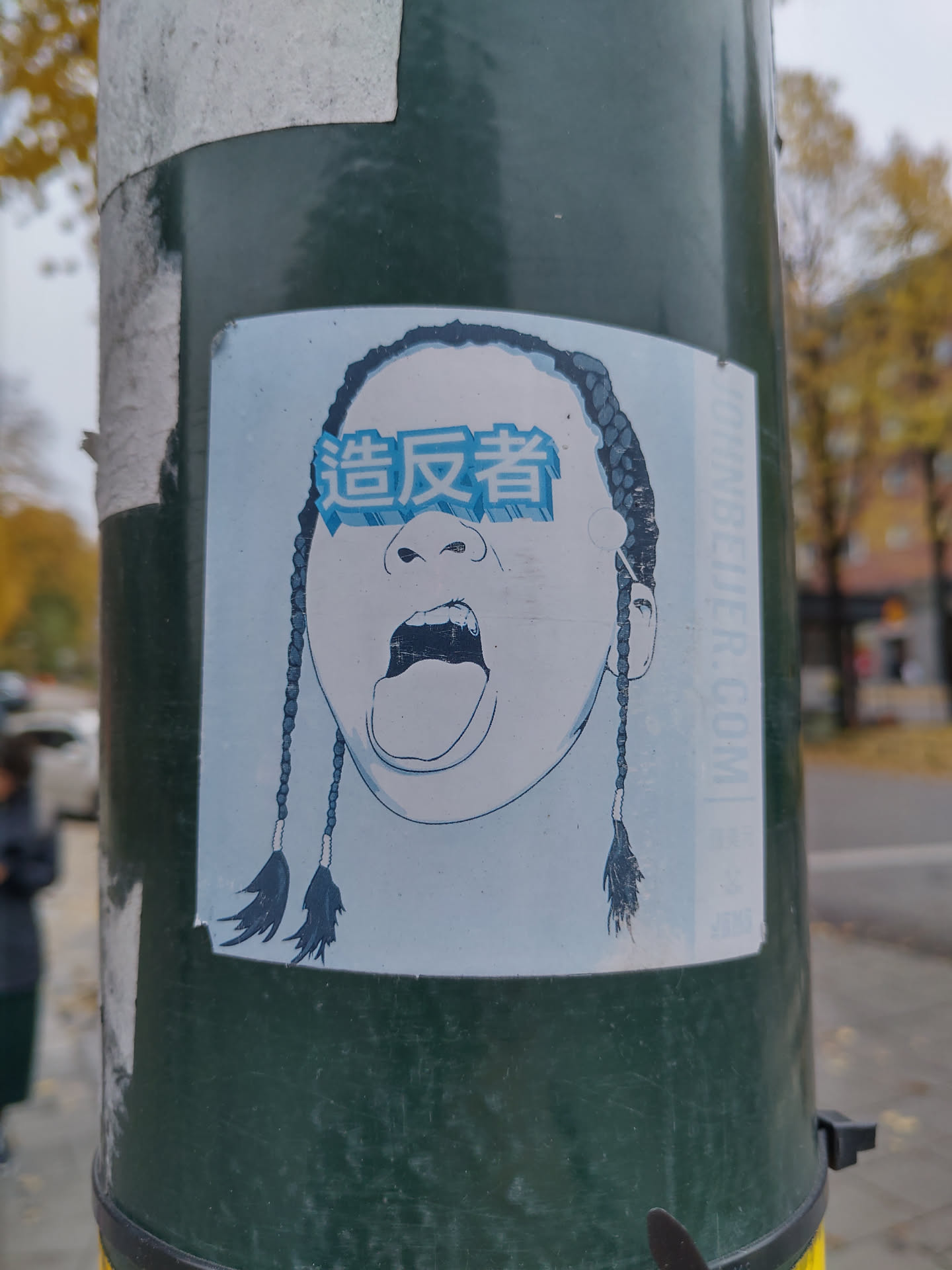 This sticker shows a close-up of a person's face, depicted in a minimalist style with dark hair styled in braids.  The eyes are covered by a rectangular shape with Chinese characters. The mouth is open in a shout or yell. The overall aesthetic is bold and slightly edgy.