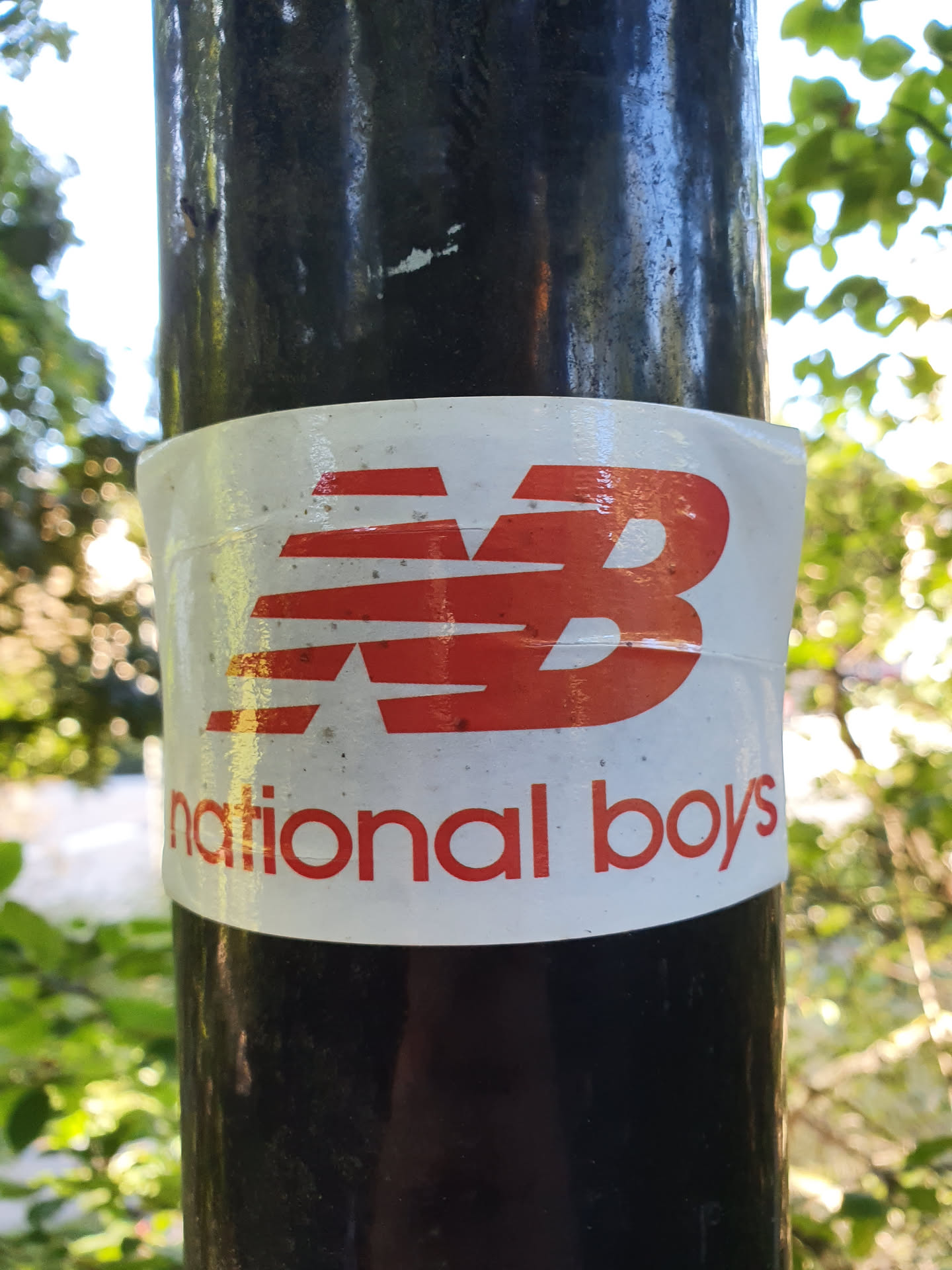 A sticker featuring the New Balance logo and the words 'national boys' affixed to a dark pole outdoors.