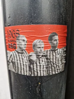A sticker featuring a black and white photo of three young men in striped shirts. The photo is set against an orange background and includes the text "1968", "H.Match", "Dag", and "146".