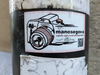 A sticker featuring a drawing of a camera, the photographer's name, and a QR code. The style is minimalist and slightly vintage.