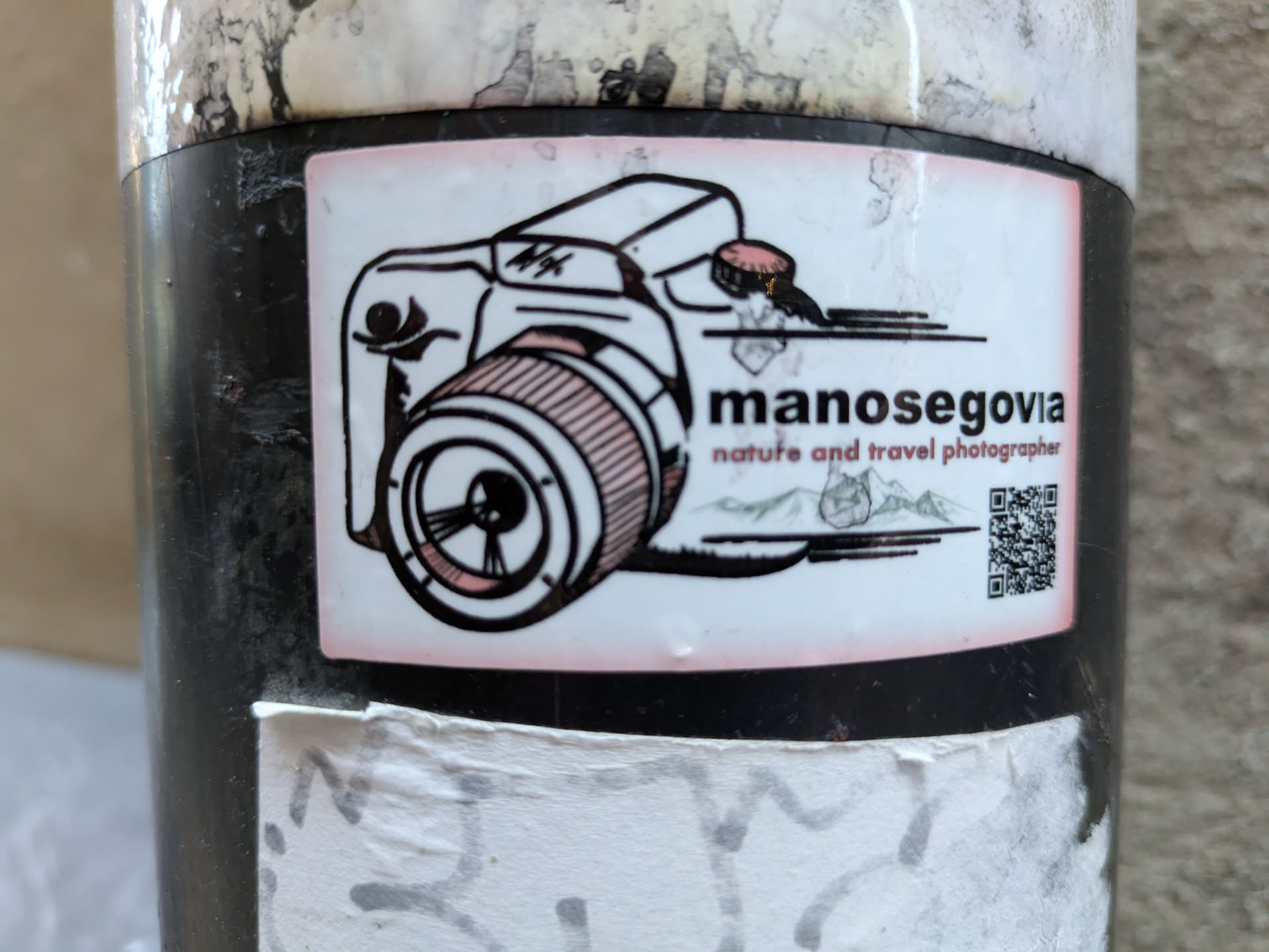 A sticker featuring a drawing of a camera, the photographer's name, and a QR code. The style is minimalist and slightly vintage.