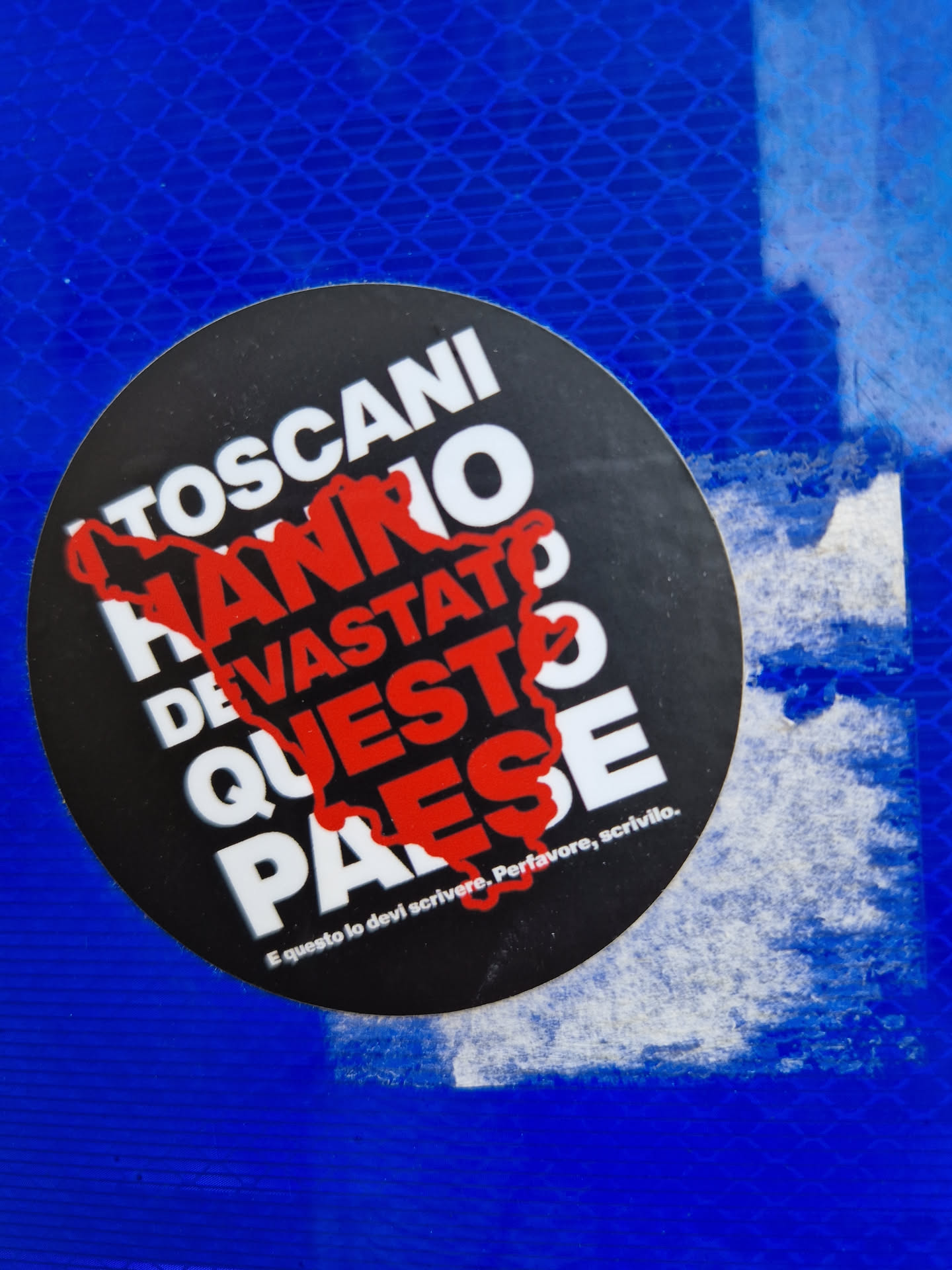 A black and red circular sticker with Italian text. The text translates to: "Tuscans have devastated this country."  A smaller text at the bottom reads: "And this you must write. Please, write it."