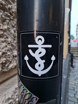A black and white sticker of an anchor on a black pole. The anchor is stylized and has a simple design. The sticker is square with rounded corners.