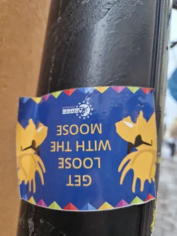 A blue sticker with two yellow moose and the text "GET LOOSE WITH THE MOOSE". There is a colorful stripe at the top and bottom of the sticker. It appears to be a sticker for a European Union-related event.