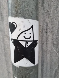 A black and white sticker featuring a cute, smiling, star-shaped character in a tuxedo holding a heart-shaped balloon. The sticker is affixed to a metal pole. The style is minimalist and charming.