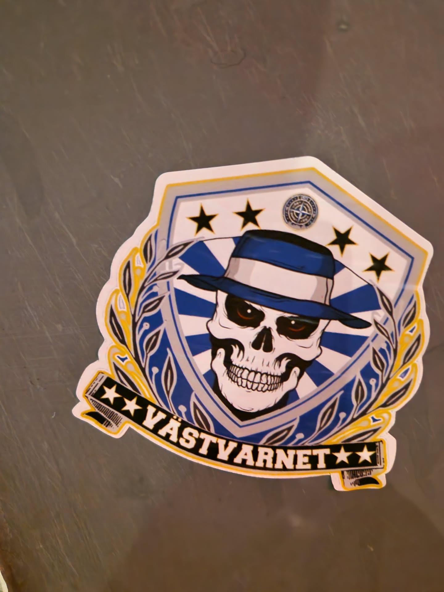 This sticker features a skull wearing a hat, surrounded by a shield with stars.  The text at the bottom reads "VASTYARNET". The style is graphic and bold, with a combination of blue, white, and yellow colors.