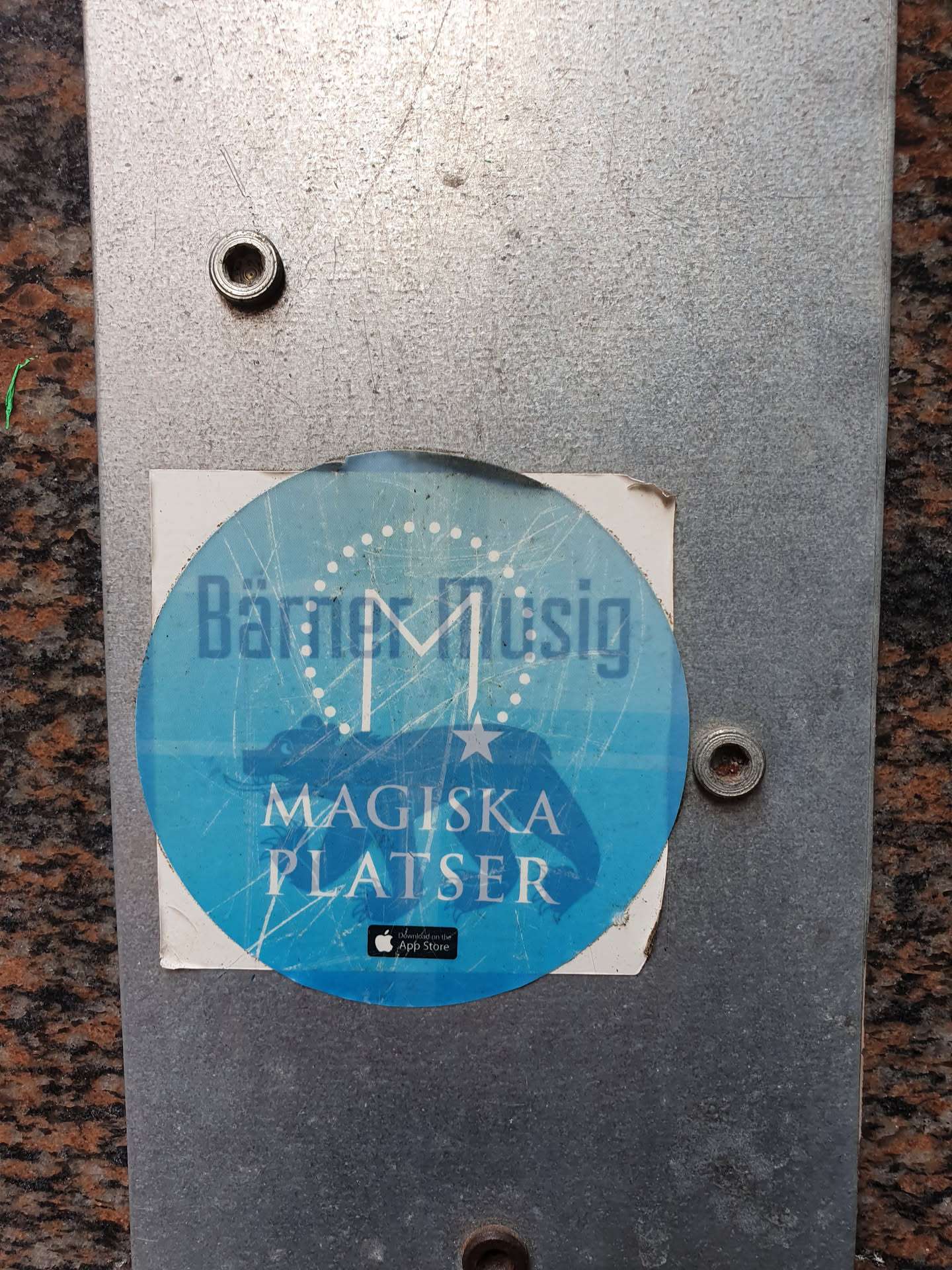 Round blue sticker with the text "Bätmer Musik" and a stylized letter M in the center. Below it, it says "Magiska Platser" and features an Apple App Store logo. The design includes a star and a map-like image.