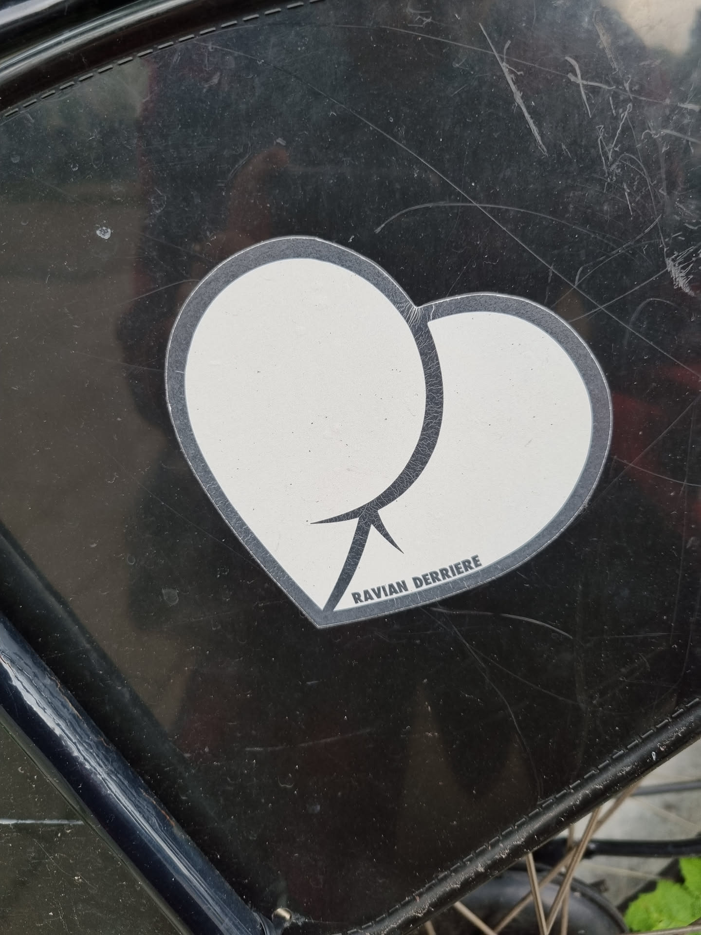 A black and white sticker depicting two overlapping circles forming a heart shape. The text "RAVIAN DERRIERE" is visible at the bottom of the sticker.