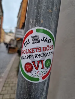 A sticker with a QR code, text in Swedish, and a design featuring thumbs up and down, along with images of biceps. The text translates to "The People's Voice - The Button Pushers VI".