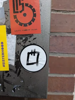 Street sticker A round sticker with a thin black border surrounding a white center. Inside, a minimalist abstract symbol or glyph is drawn in textured, dry black brushstrokes, resembling a square outline with two vertical hatch marks extending upwards from the top edge.