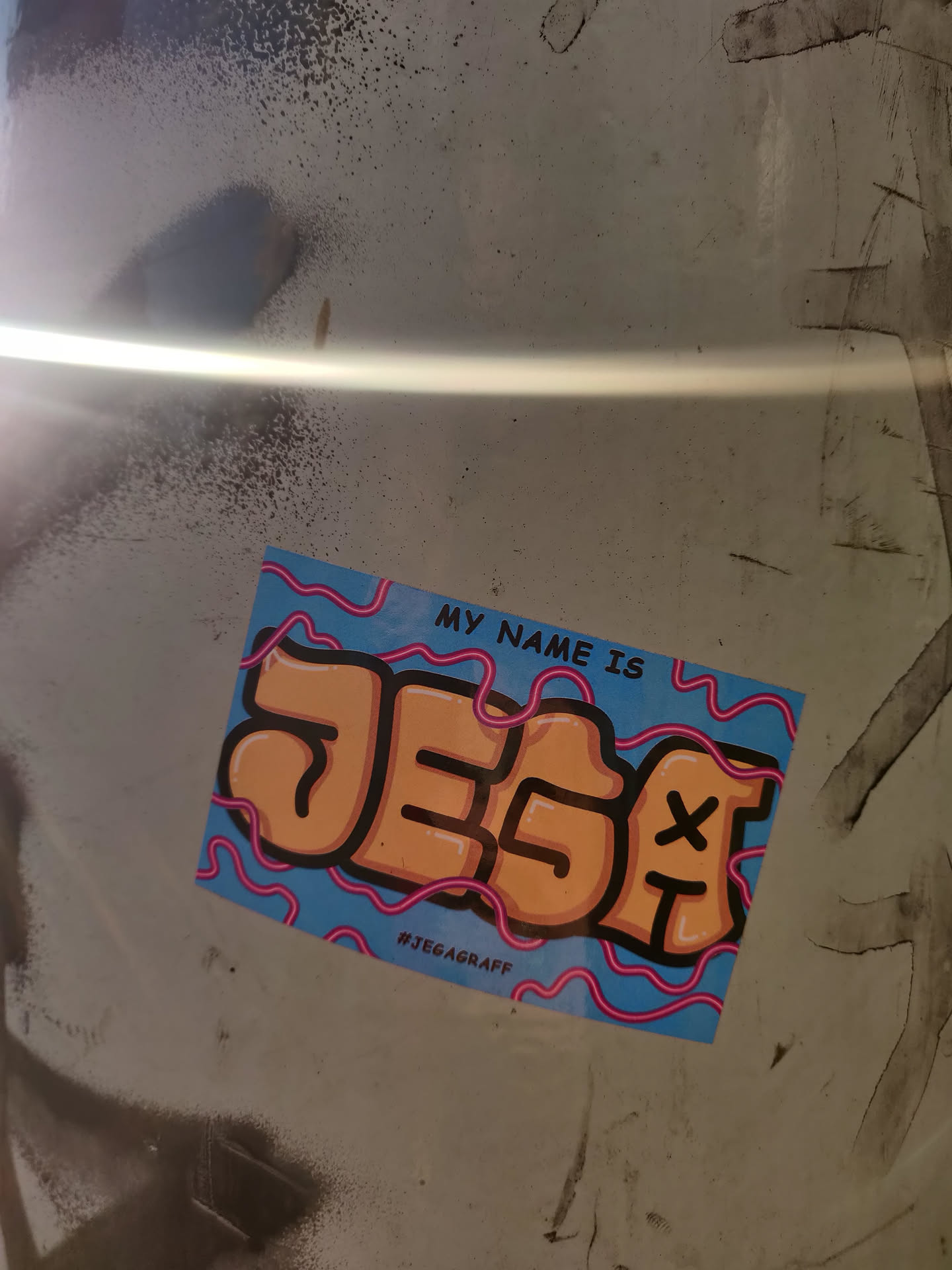 A sticker with a stylized name JESA in orange letters on a light blue background with pink lines. The text "My name is" is written on the top. The hashtag #JEGAGRAFF is visible at the bottom.