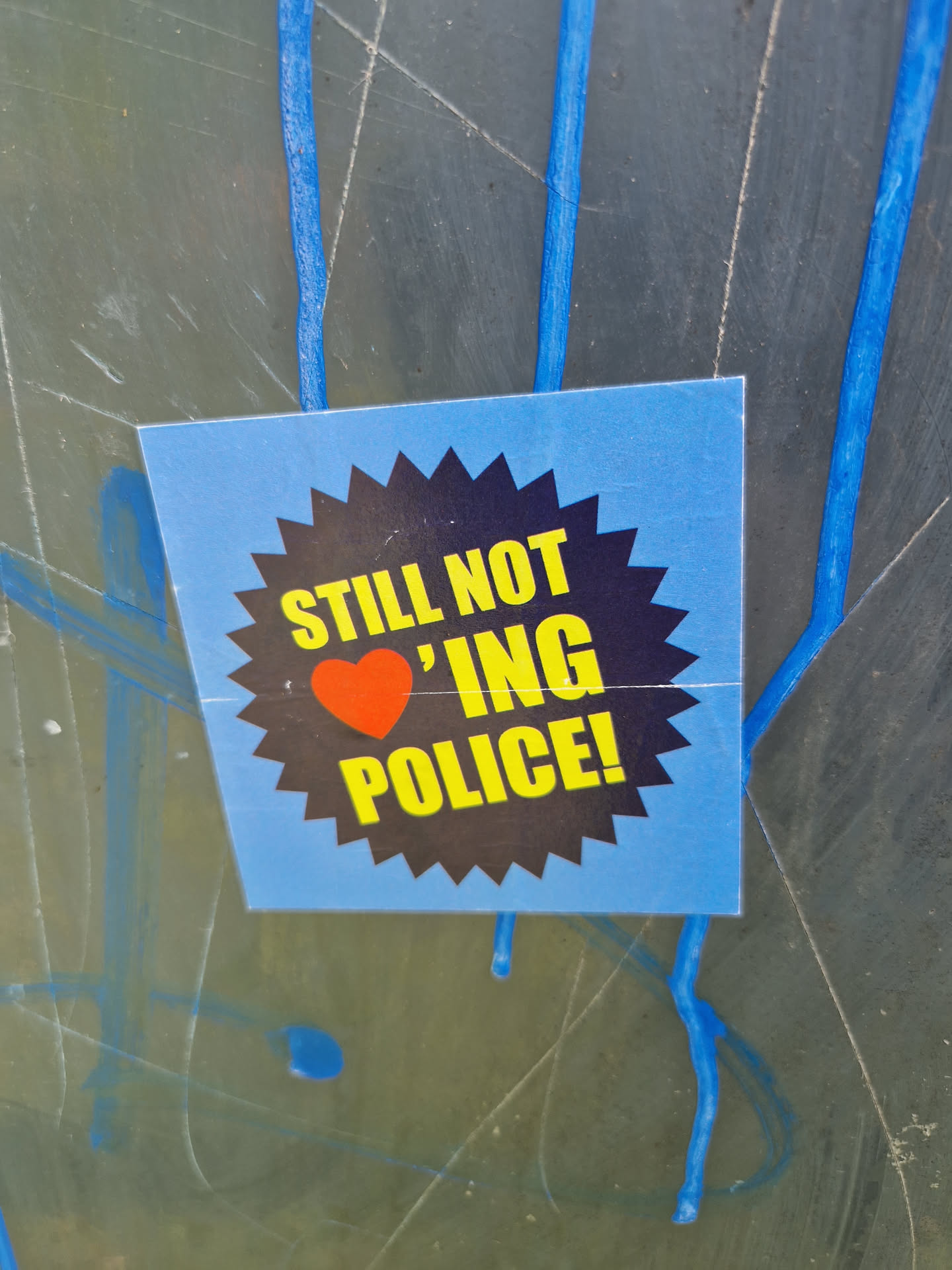 A blue sticker with a black sunburst graphic. The text on the sticker says "STILL NOT \u2764\ufe0f 'ING POLICE!"