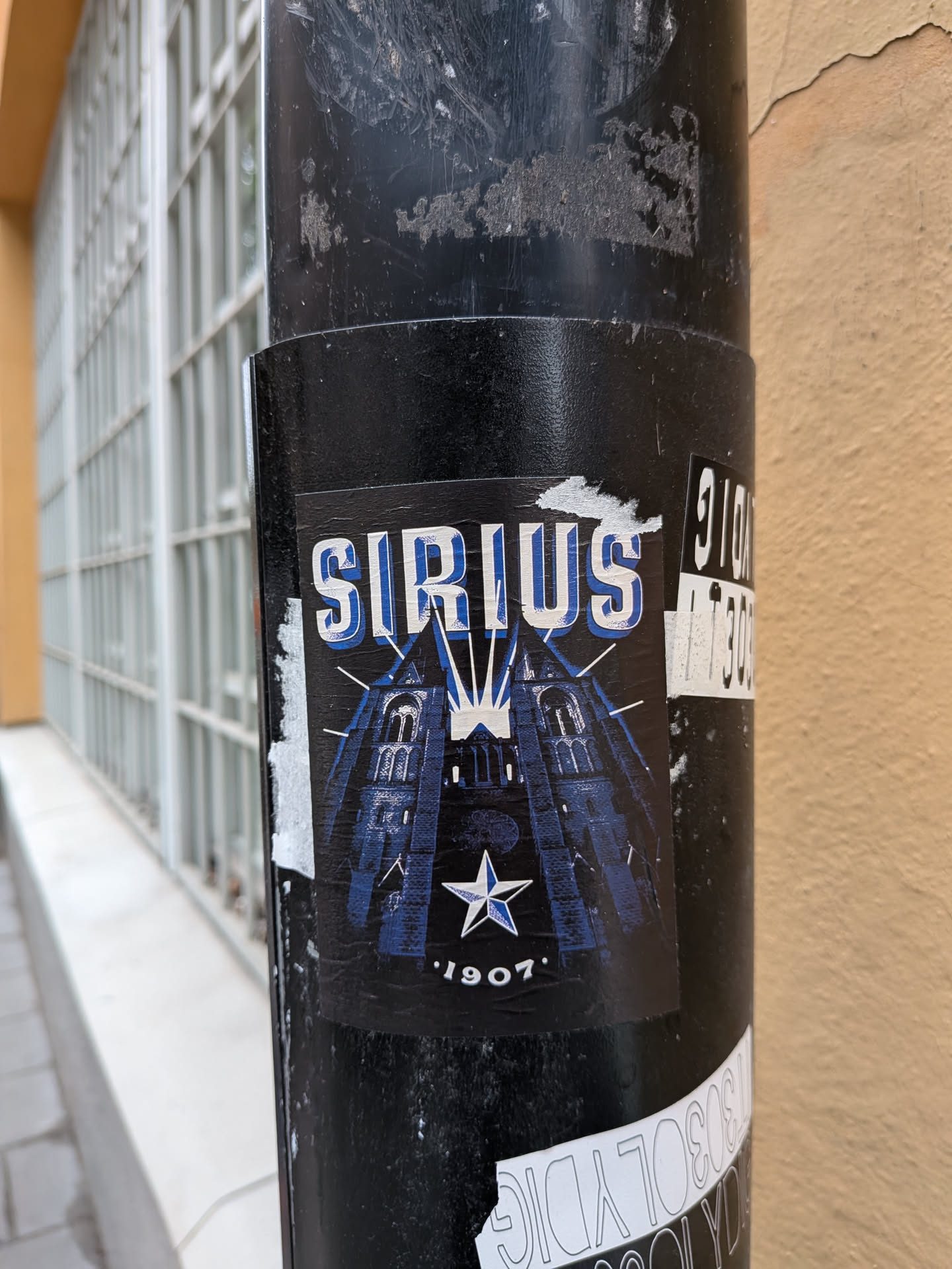 A rectangular black sticker depicting a blue-toned illustration of Uppsala Cathedral's twin spires. The word 'SIRIUS' is displayed at the top in bold, blue-and-white block letters with light rays emanating from behind. A blue and white five-pointed star sits above the year '1907' at the bottom.