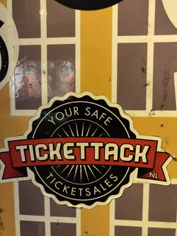 Street sticker Close-up of a Tickettack sticker on a wall. The sticker is black and red with the text "Tickettack" prominently displayed. The text "Your safe ticketsales" is also visible on the sticker.