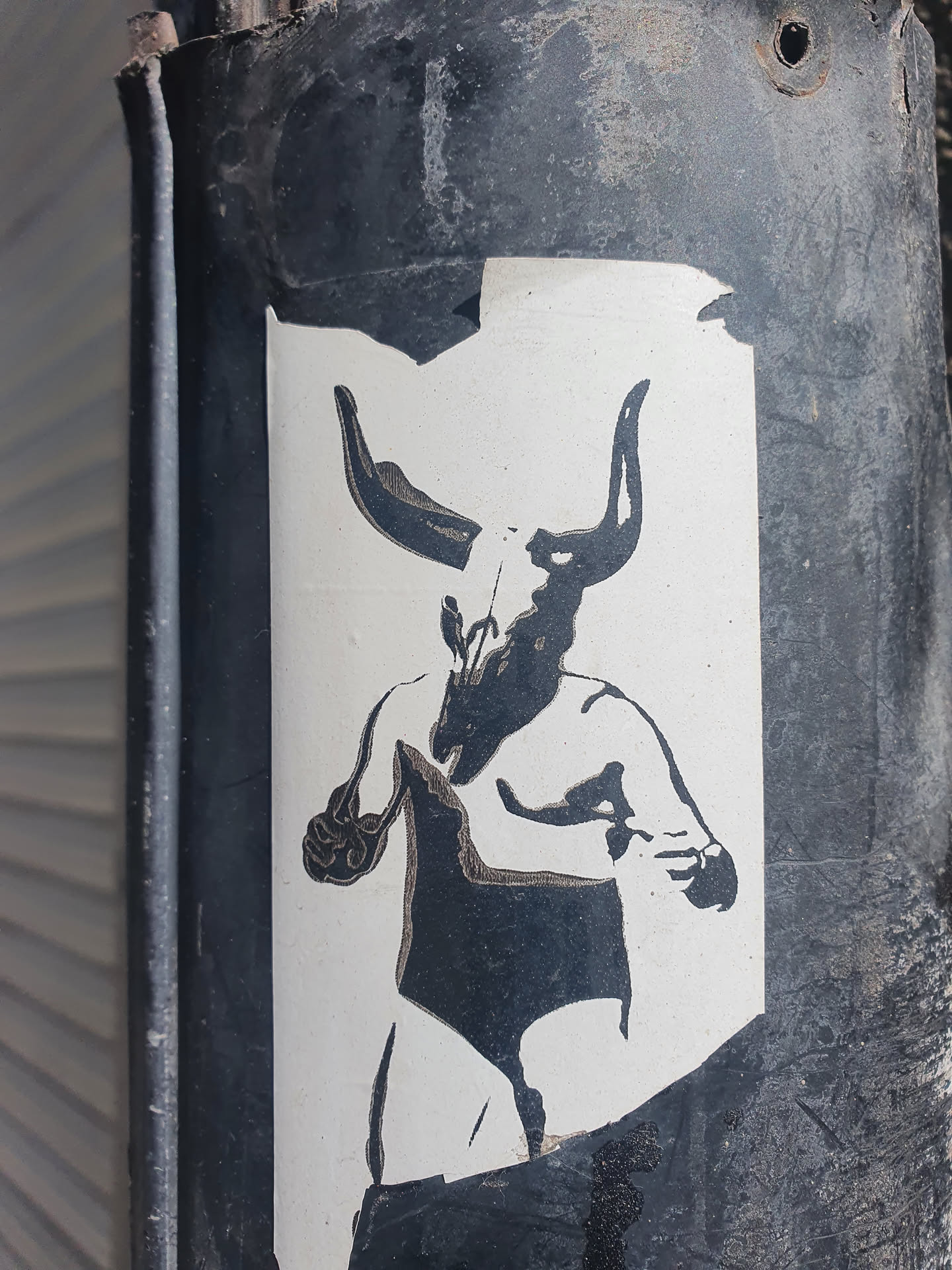 Black and white sticker of a wrestler with a bull skull for a head. The sticker is slightly damaged around the edges. The style is reminiscent of dark art and stencil art.