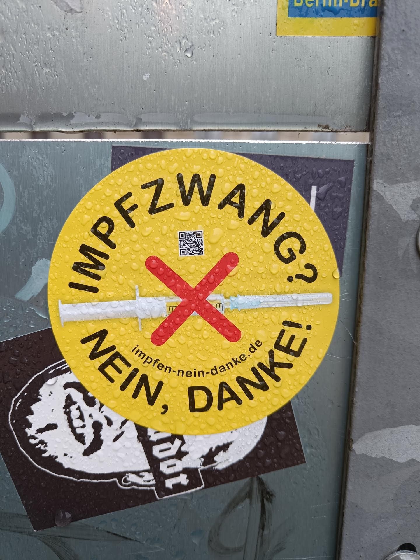 A yellow round sticker with the text "Impfzwang Nein, Danke!" and a crossed-out syringe.  It also contains a QR code linking to impfen-nein-danke.de. The sticker appears to be expressing opposition to mandatory vaccination.