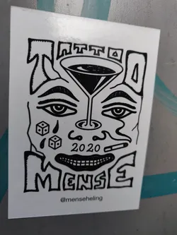 Black and white sticker with a stylized face, a martini glass, dice, and a cigarette. The text 'Tattoo MenSe' and '2020' are visible.  The artist's Instagram handle is included at the bottom.