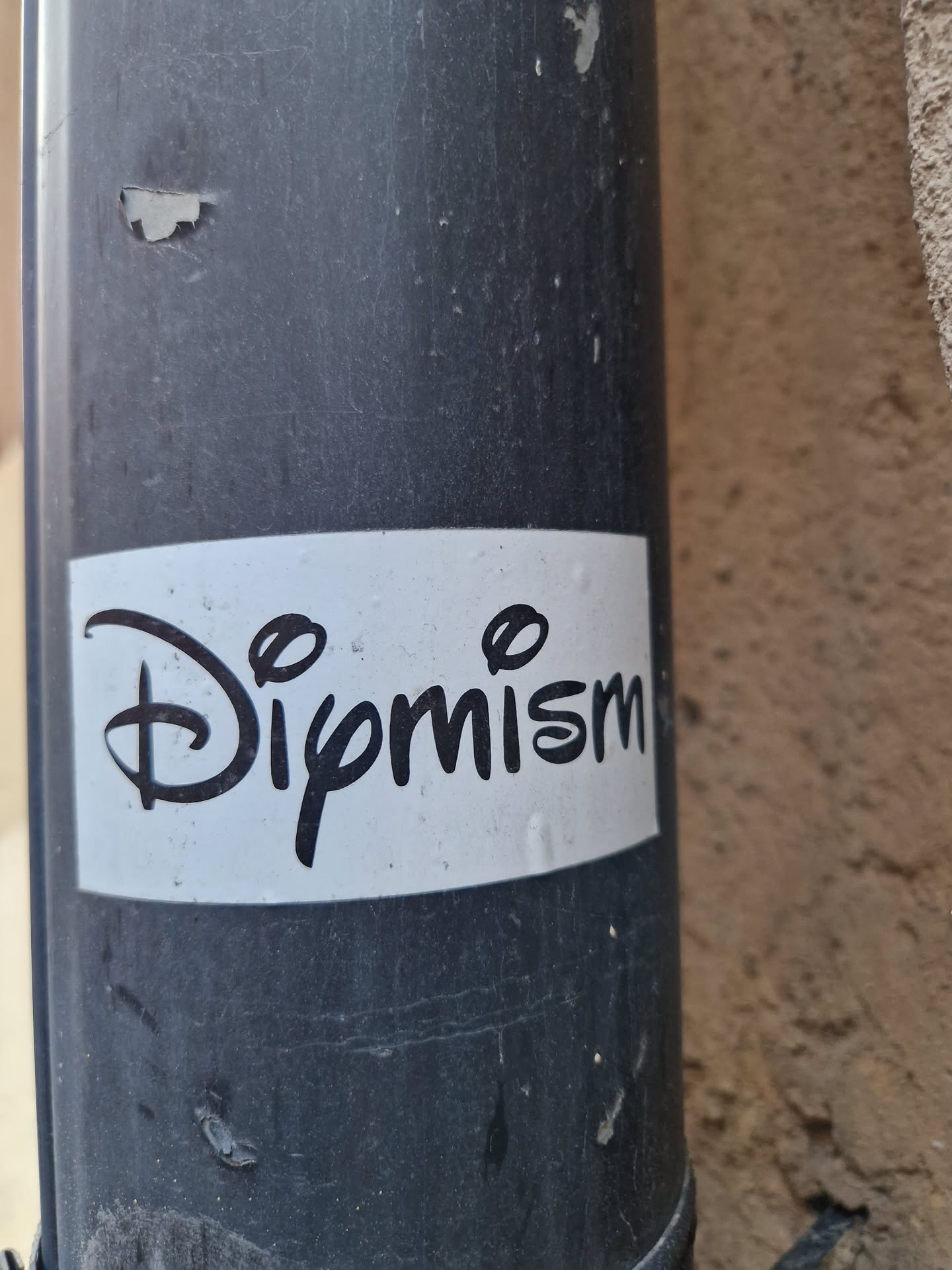 A white sticker with black text on a dark grey pipe. The text is stylized and says "Dipmism".