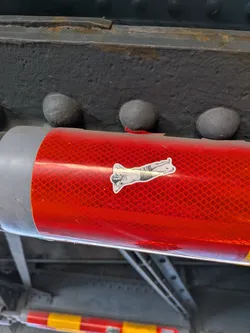 The sticker is a black and white illustration of a human figure lying down, with their head propped up on their hand and their legs bent. The figure is depicted in a stylized, somewhat abstract manner. The sticker has a white border and is placed on a red, reflective surface with a diamond pattern.