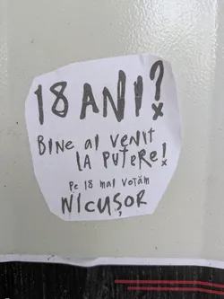 The image shows a hand-written sticker with a political message in Romanian, featuring the name 'Nicușor'. The sticker appears to be promoting a candidate, as it mentions voting on May 18th. The overall aesthetic suggests a grassroots or DIY campaign effort.