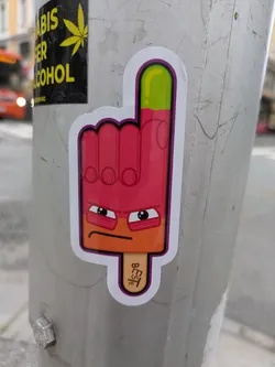 A vibrant sticker featuring an anthropomorphic ice cream popsicle shaped like a hand with the index finger raised. The popsicle is primarily bright pink/red with an orange lower section forming a face, and a lime green tip on the raised finger. It has a distinctive grumpy or determined expression with thick eyebrows and wide eyes. The sticker has a white border with a purple inner outline. A wooden popsicle stick protrudes from the bottom.