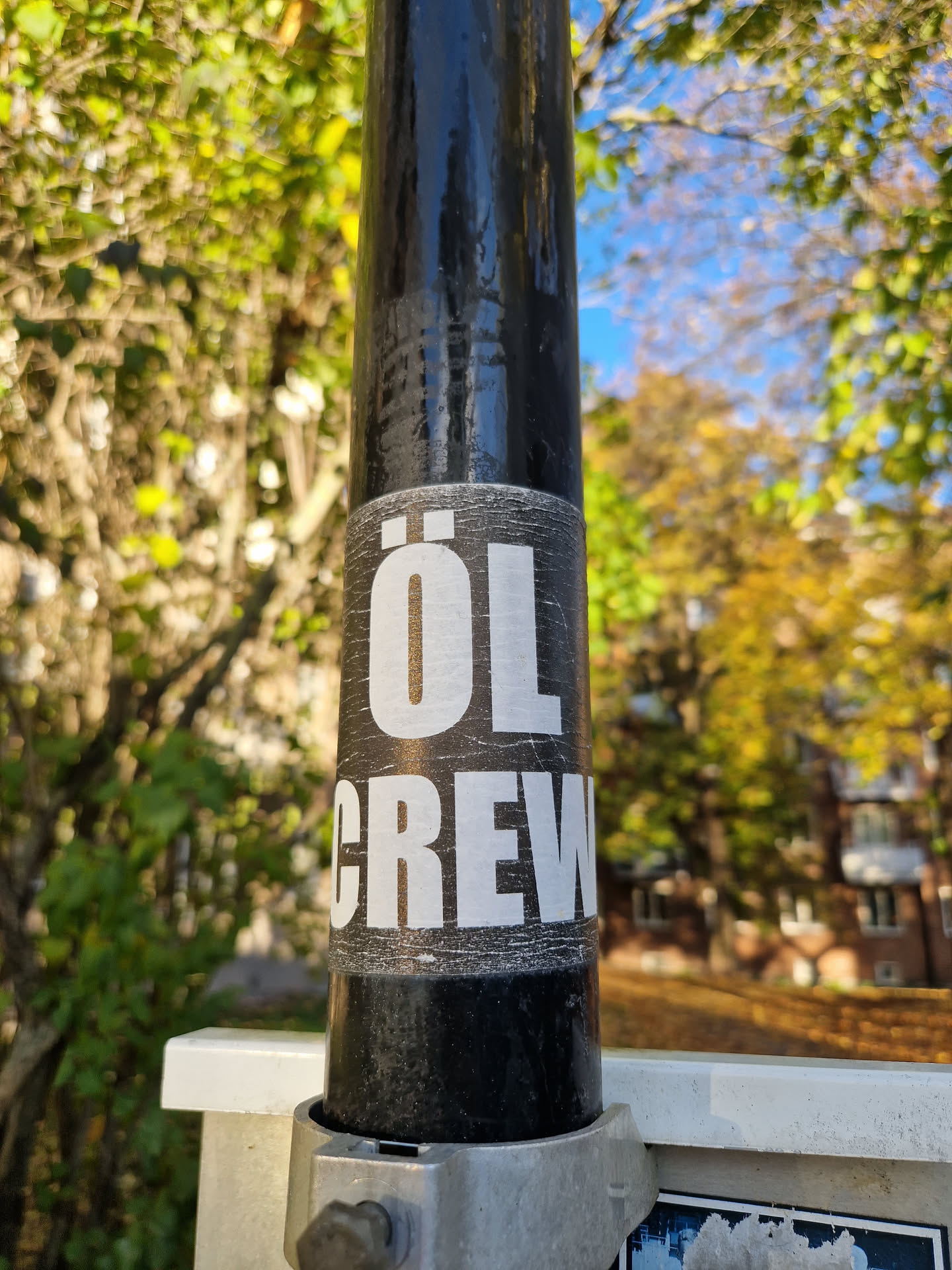 A black and white sticker with the text "ÖL CREW" on it is attached to a black pole. The sticker shows some wear and tear.