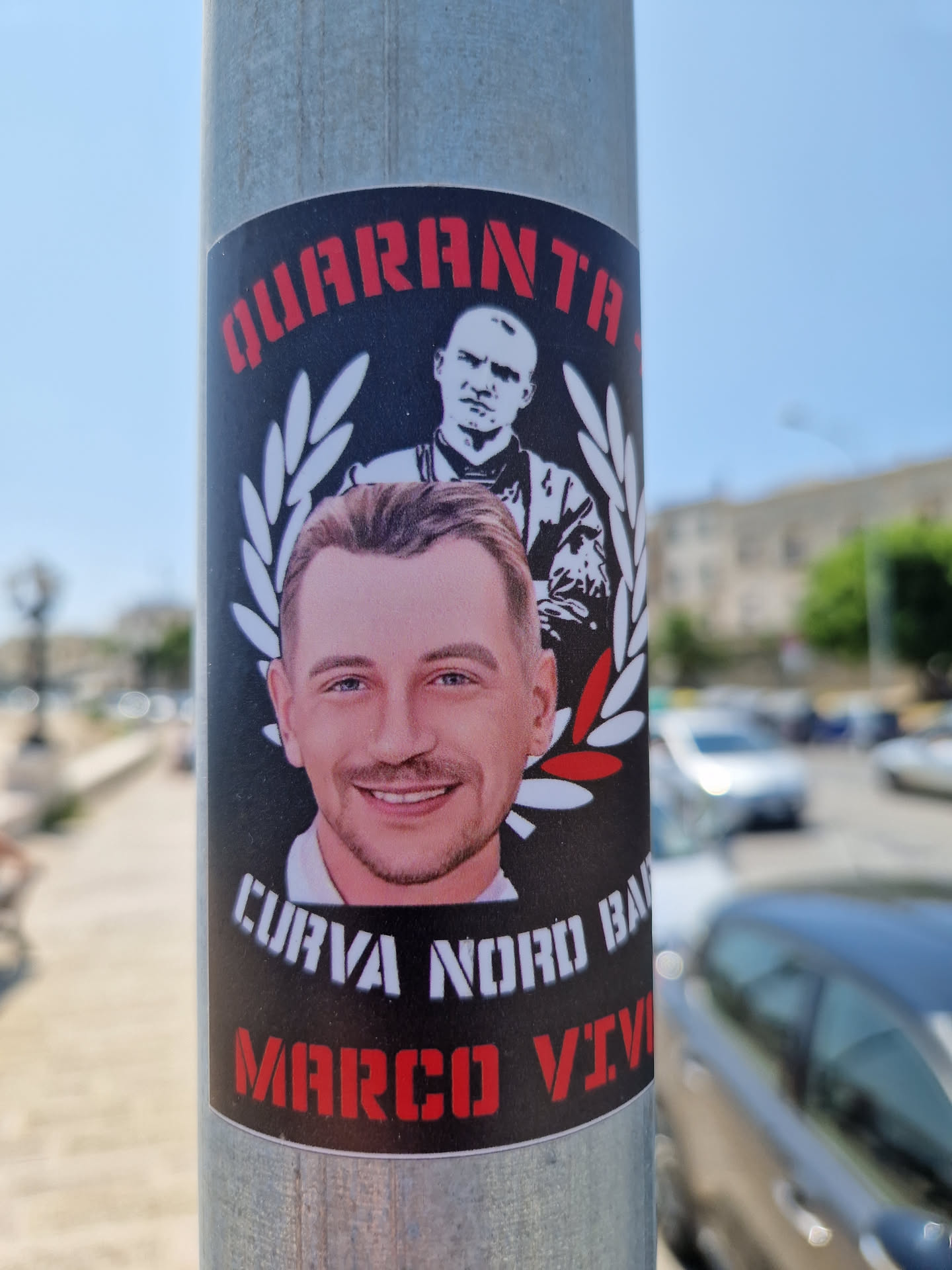 A sticker featuring a portrait of Marco, with the text "QUARANTA" at the top, "CURVA NORD BARI" at the bottom, and a laurel wreath.  Another person is in the background.  The words "MARCO VIVO" are also present, suggesting a tribute.