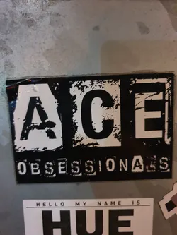 Black and white sticker with the text "ACE OBSESSIONALS" in a grunge style. There is another sticker below that says "HELLO MY NAME IS HUE"
