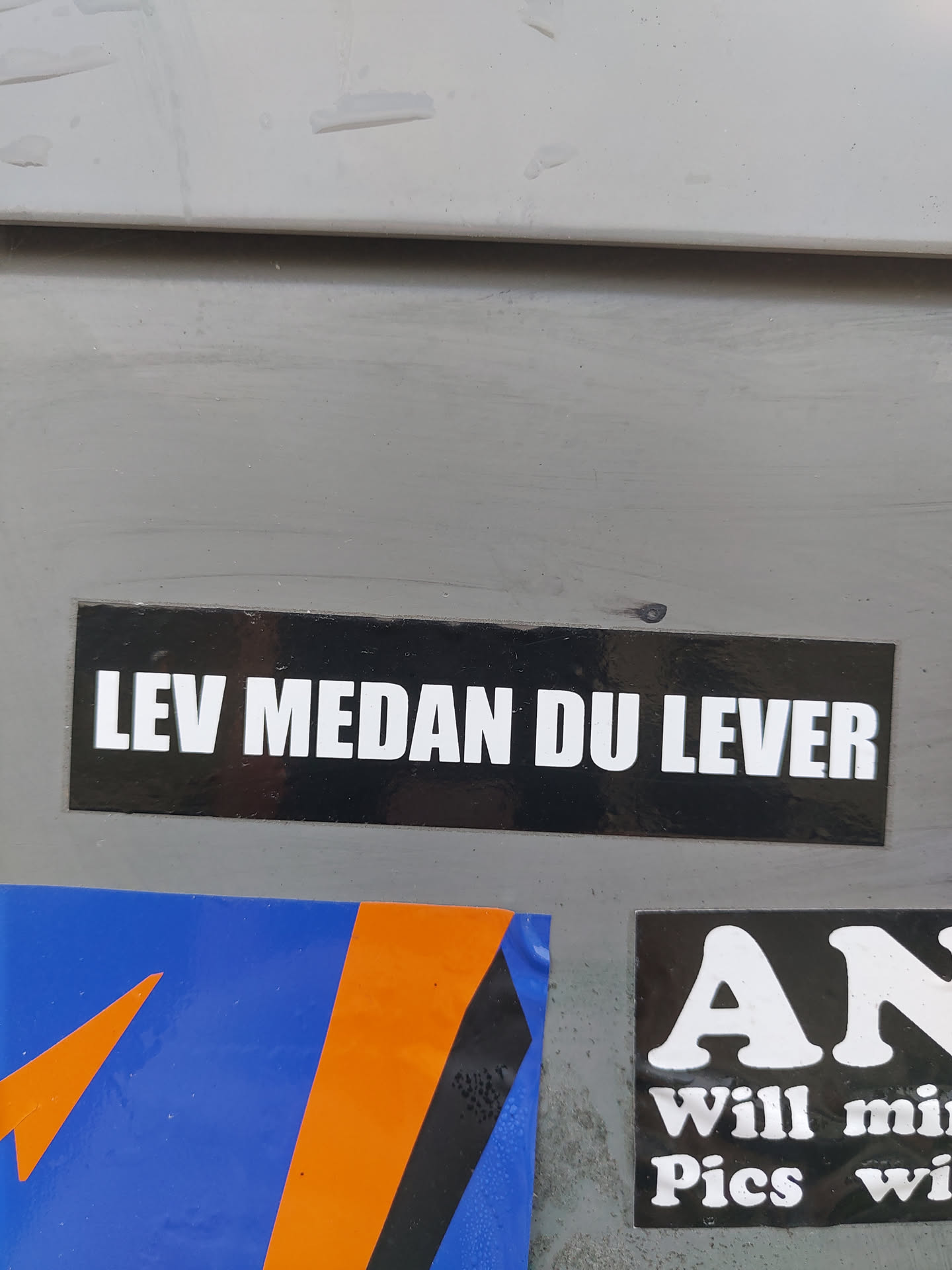 A black rectangular sticker with white text. The text says "Lev Medan Du Lever", which is Swedish for "Live While You Live."