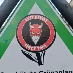 A round sticker featuring a devil mascot with the text 'East Devils Since 2001'. The sticker is affixed to a triangular sign.