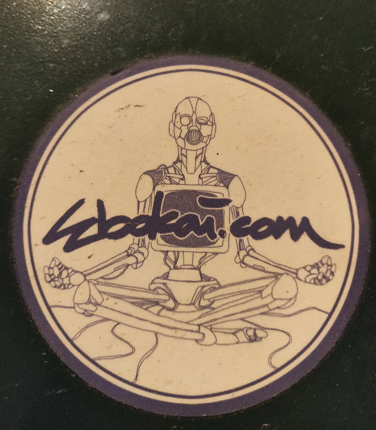 Round sticker featuring a robotic figure in a meditative pose. The robot has a screen for a chest and is drawn in a vintage style.  The website zbdkai.com is written under the illustration.
