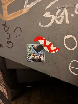 Street sticker A square sticker depicting the character Cell Jr. from Dragon Ball Z in a chibi/stylized art style. The character is light blue with black spots, red eyes, and dark purple/black accents, sticking its tongue out and waving its hands playfully next to its face. Japanese manga sound effect text appears vertically along the left edge against a pale green background.