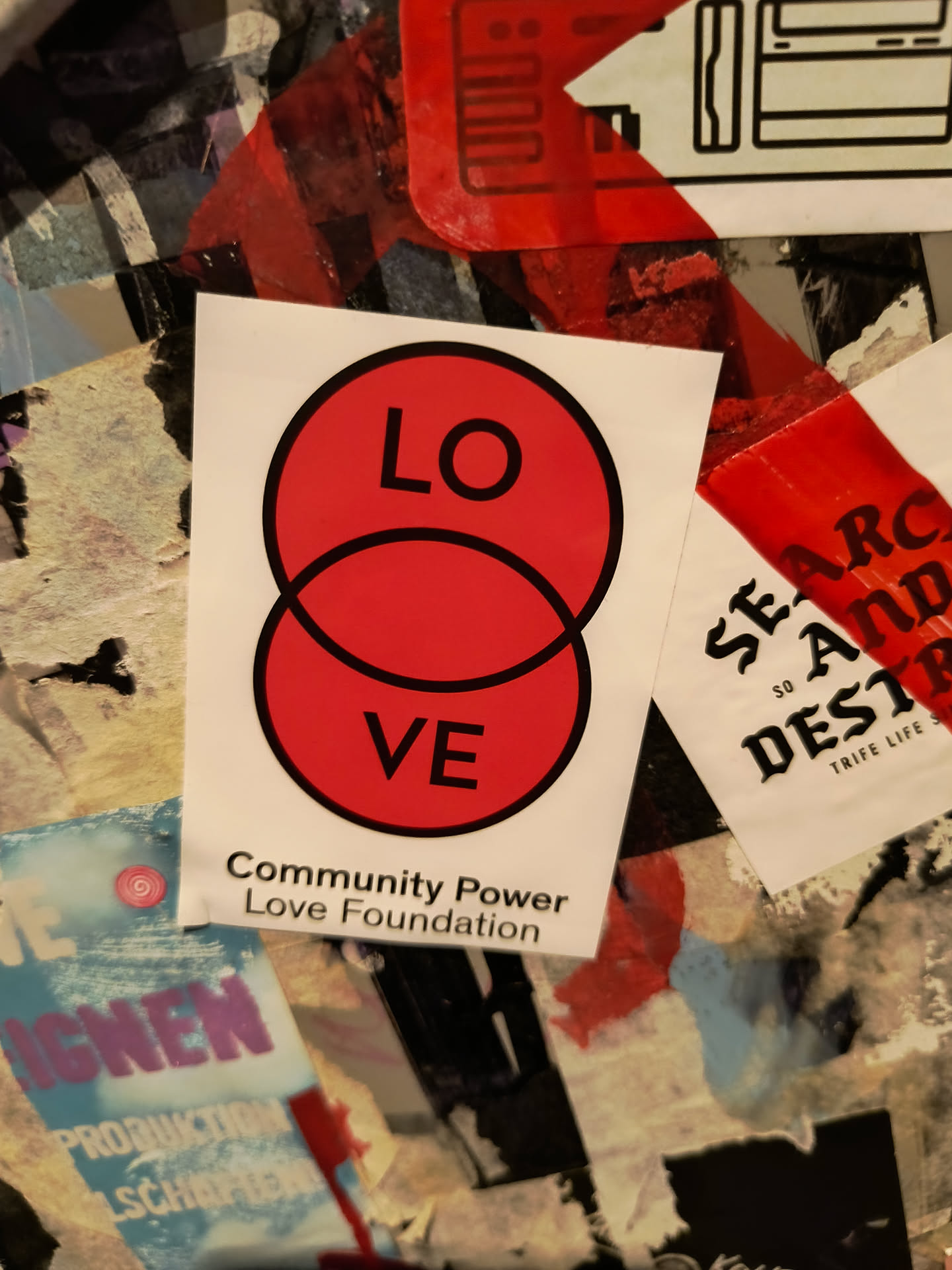 A red and white sticker with the word "LOVE" split into two circles. It also contains the text "Community Power Love Foundation".