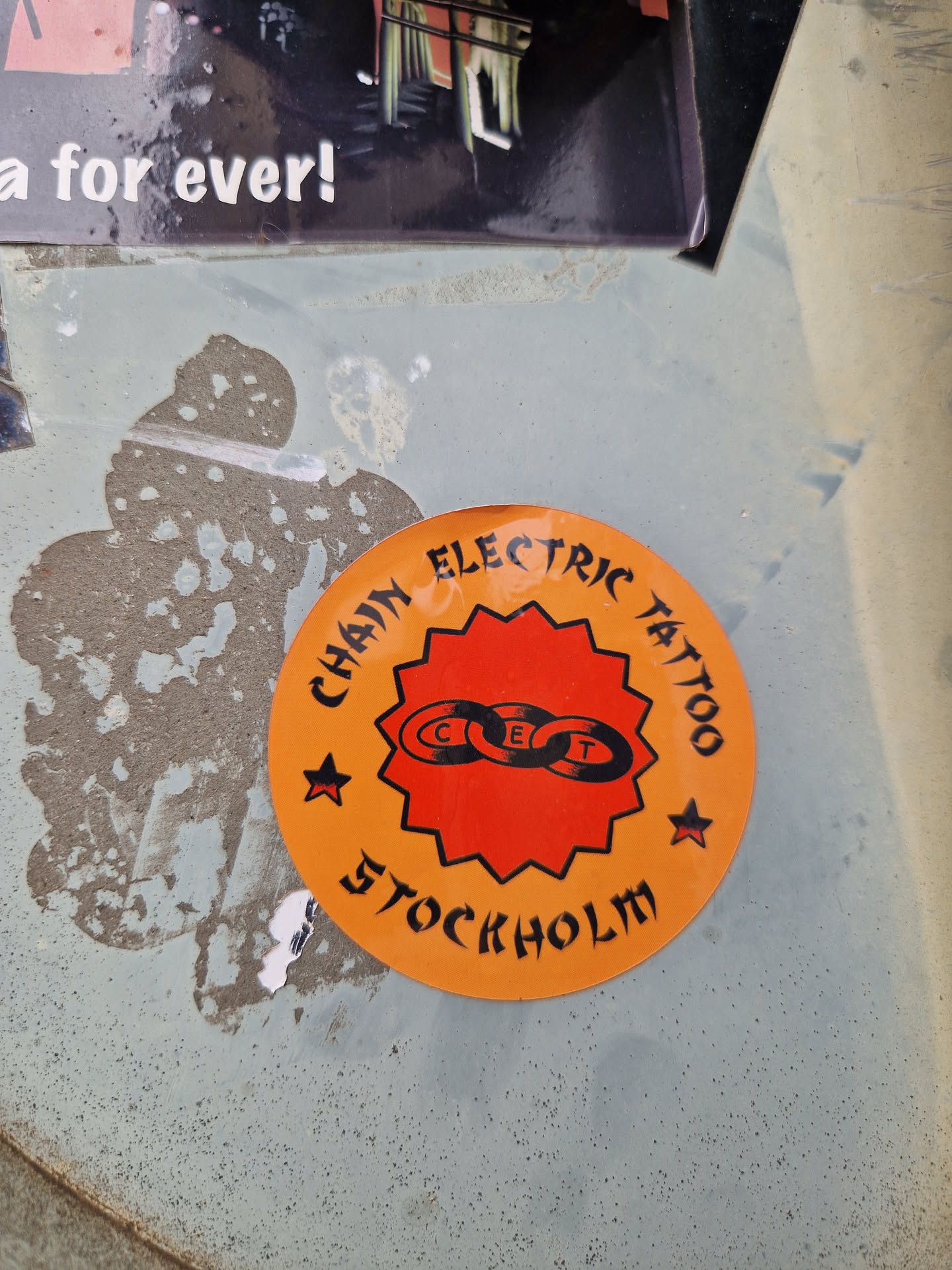Orange circular sticker with black text and logo.  The text reads: "Chain Electric Tattoo Stockholm". The logo is a stylized chain link. 