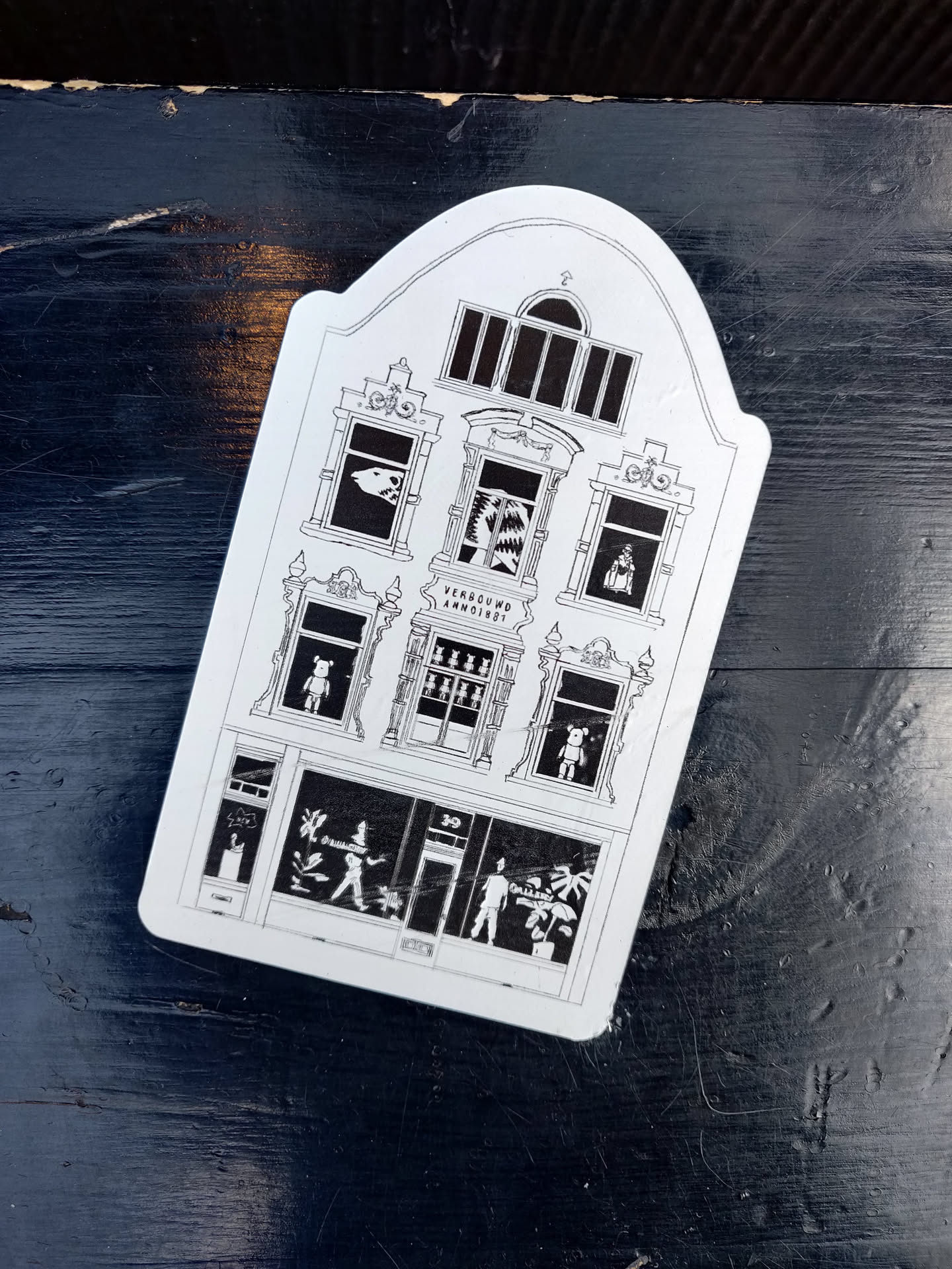 This sticker features a black and white illustration of a building with arched windows and a storefront. The windows show various scenes, including a shark, a bear, and people shopping. The building number is 30. 