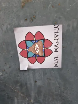 A sticker featuring a stylized image of a pile of poop with an eye in the center, set within a colorful mandala-like design. Hebrew text is visible on the sticker's side.