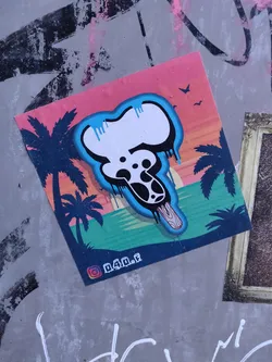 A sticker featuring a melting ice cream graphic with a skull design, set against a vibrant sunset beach backdrop. The style is reminiscent of graffiti art with a playful twist.