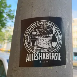 Black and white sticker with a logo. The logo contains a bag, bottles, a scale, and a champagne bottle inside a Greek fret border. The text Alleshabensie and est. 2016 are written below the logo.