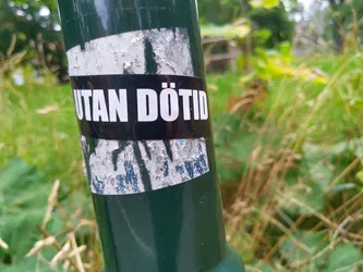 A worn sticker on a green pole. The text on the sticker says "UTAN DÖTID" which translates from Swedish to English as "WITHOUT DEATH".