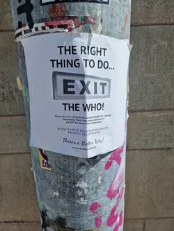 A sticker on a pole advocating for exiting the World Health Organization. It includes hashtags and a website address.