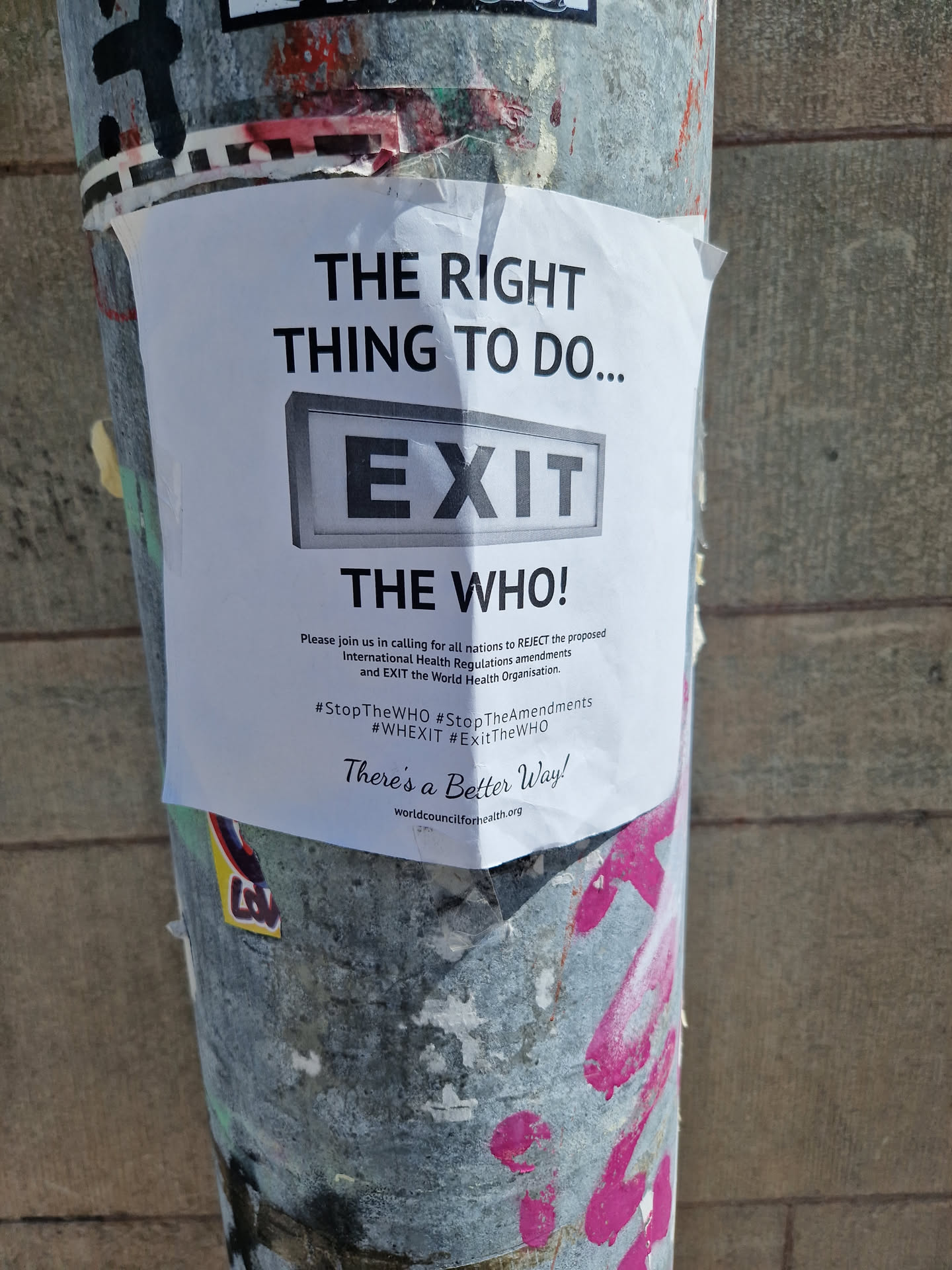 A sticker on a pole advocating for exiting the World Health Organization. It includes hashtags and a website address.