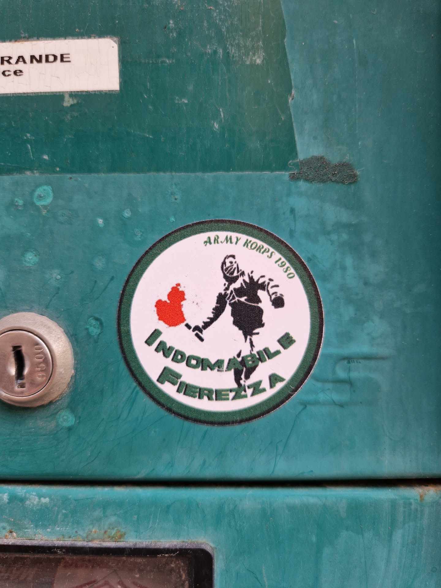 A round sticker featuring a silhouette of a person holding a burning object, with the text "Indomabile Fiertezza" and "Army Korps 1950".