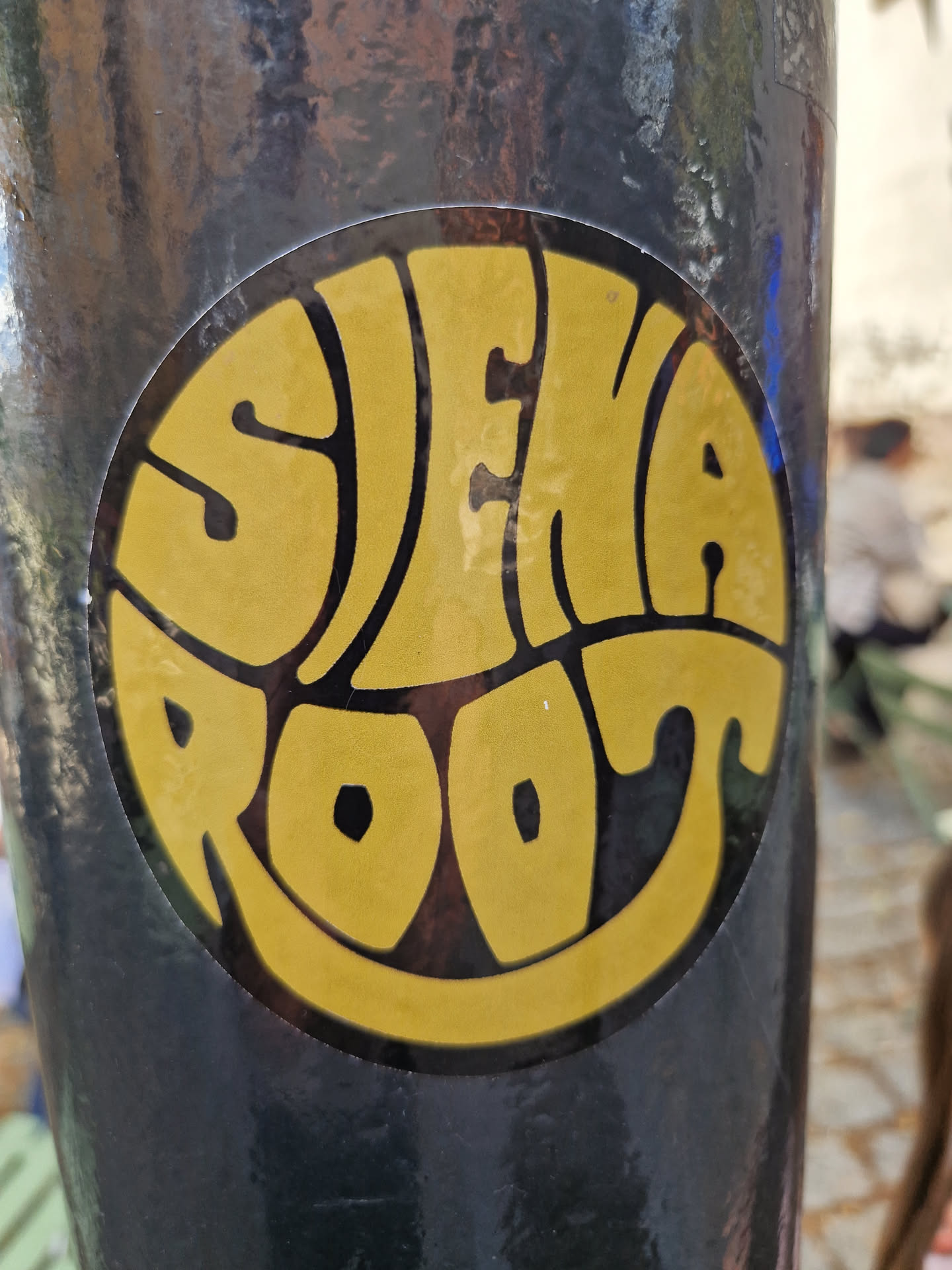 A round sticker with the words "SIENA ROOT" written in a retro, psychedelic font.  The text is yellow on a black background. The style is reminiscent of 1960s or 1970s album art.