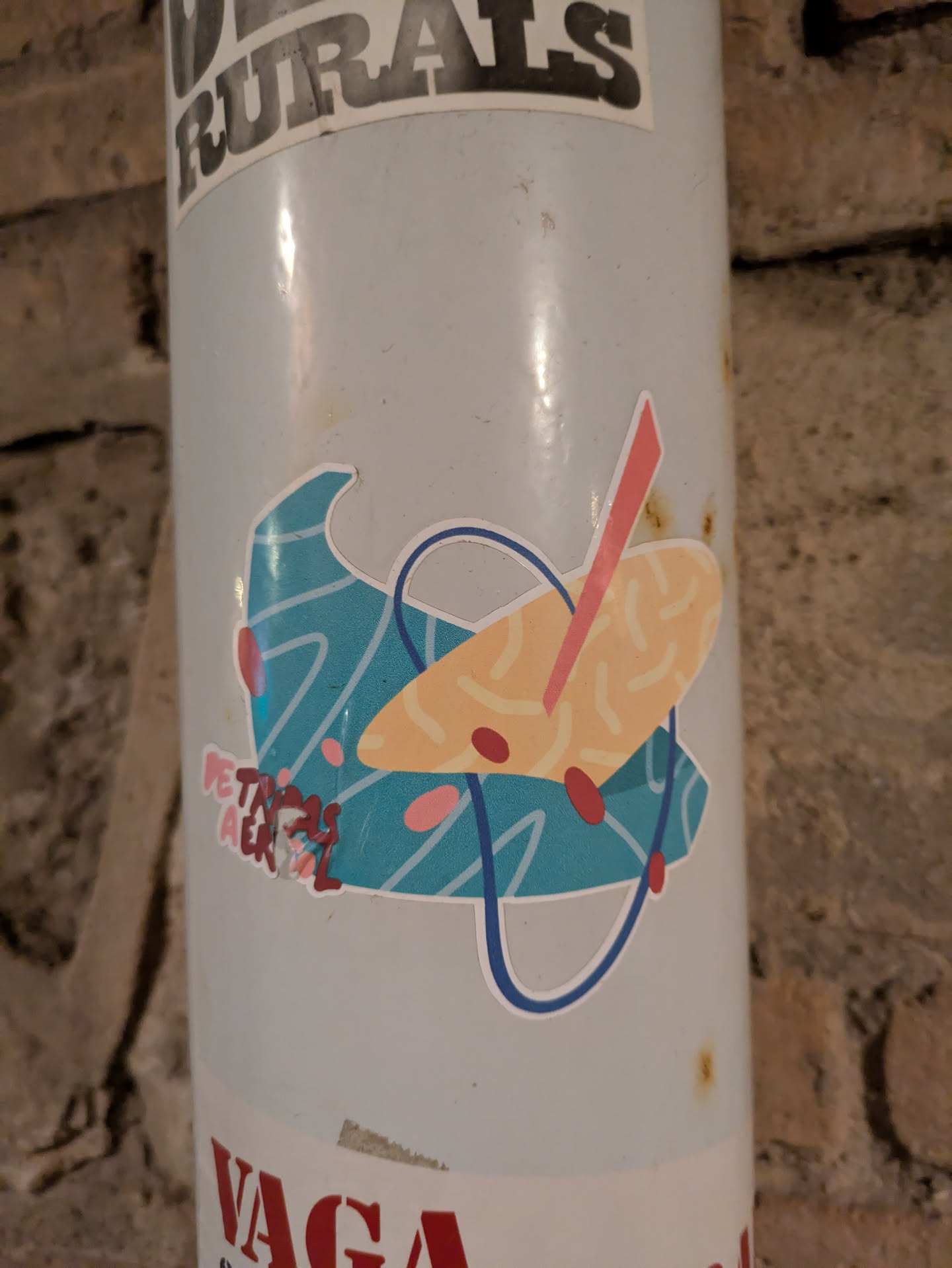 The sticker displays an abstract design with a combination of geometric shapes in blue, tan, and red. A blue wave-like form is positioned on the left, and a tan, speckled shape with a red stick stands atop it. The design is outlined with a dark blue border. Text 'DE TAS A EL' is visible at the bottom left of the sticker.