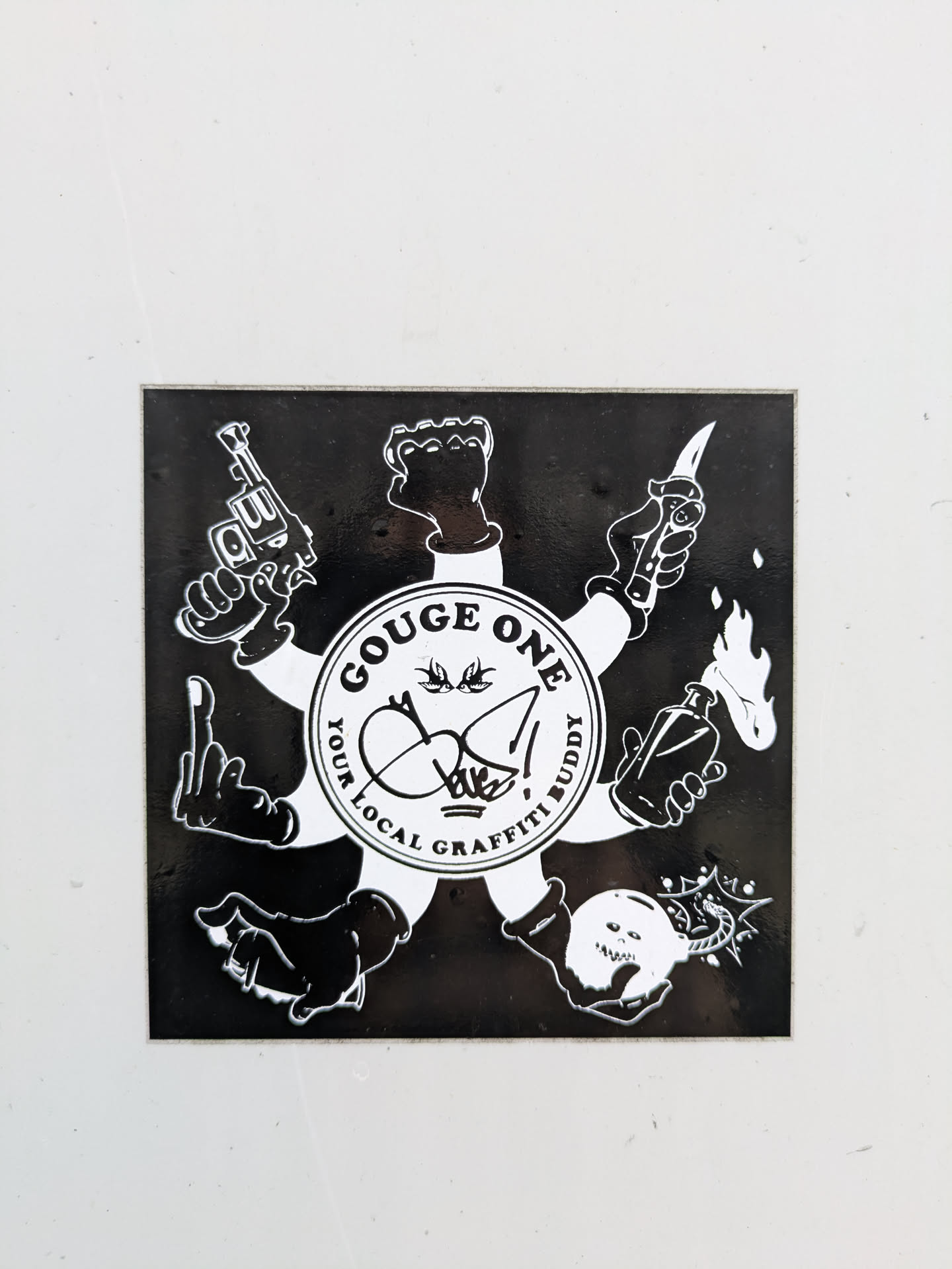 The sticker showcases a design with arms extending outwards, each hand holding a different object like a gun, knife, Molotov cocktail, and a skull. The central circle reads 'GOUGE ONE' and 'YOUR LOCAL GRAFFITI BUDDY'. The style is reminiscent of stencil art, with stark black and white contrast.