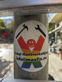 A sticker with a rainbow-colored figure holding a hammer and a wrench. The text says "Enkel HantverksHjälp" and provides an email address: info@maxfix.nu