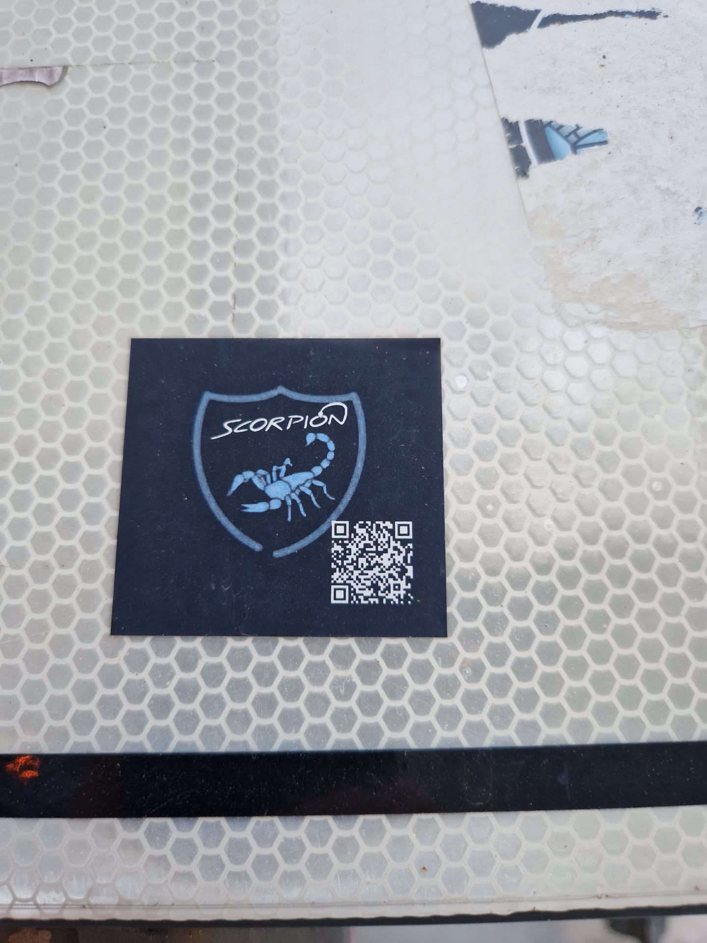 Black sticker with a scorpion in a shield and a QR code. The word SCORPION is written above the scorpion.